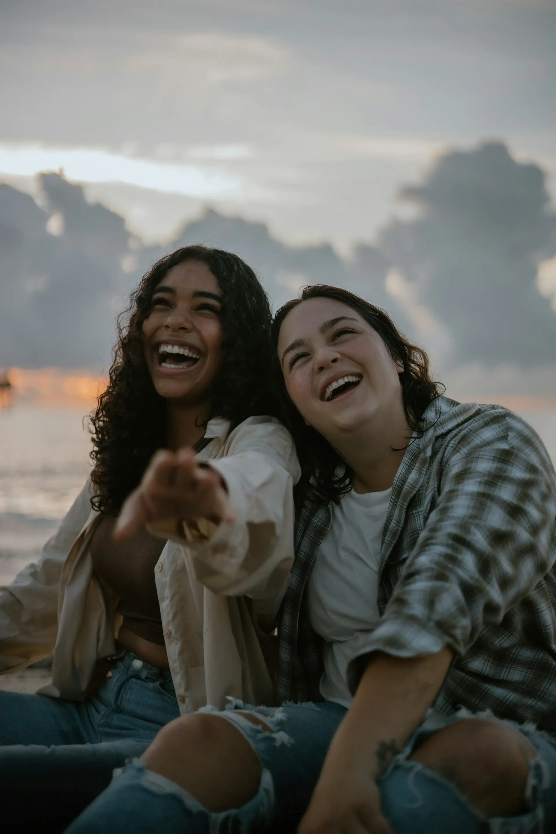 Two women on the beach pointing at the camera